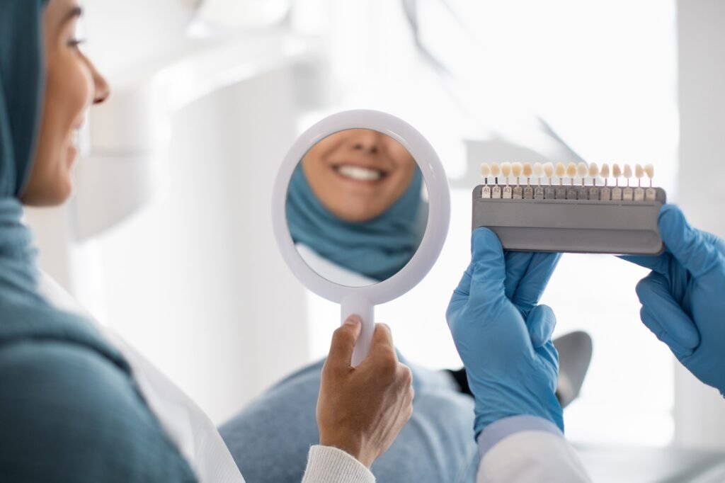 Restorative Dentistry. Muslim Female Patient Holding Mirror And Looking At Her Smile